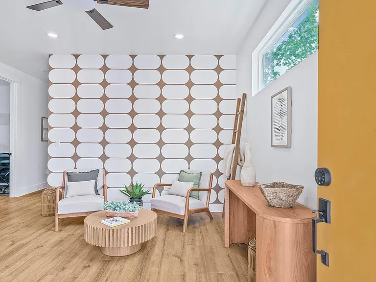 Welcoming lounge with seating for two, a statement accent wall, ceiling fan, and a large window bringing in natural light.