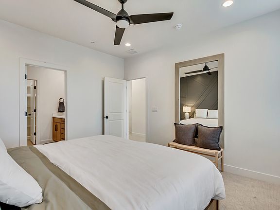 Modern bedroom with a large bed, ceiling fan, and a mirror reflecting the opposite wall. A doorway l