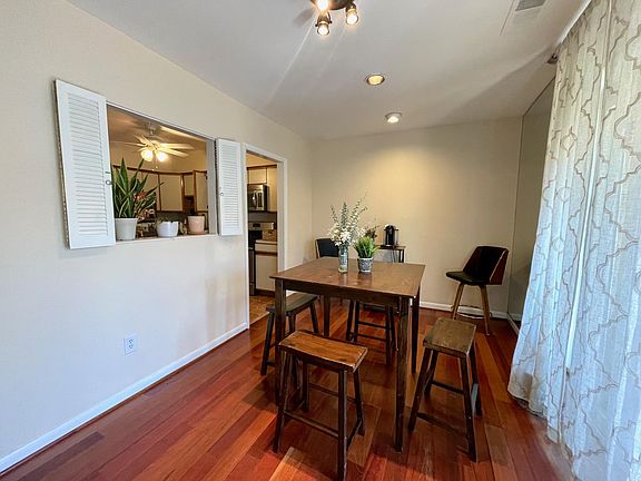 Dining space with a hightop table and four chairs and a passthrough into the kitchen - balcony attached, large windows with afternoon sunlight.