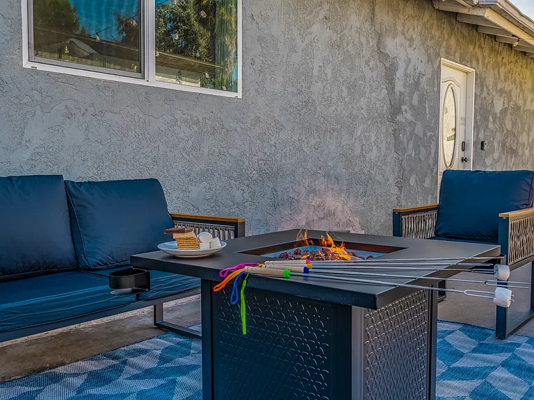 Stunning outdoor space is designed for relaxation and entertainment. A cozy fire pit takes center stage, surrounded by modern outdoor chairs with sleek black cushions and wooden armrests.