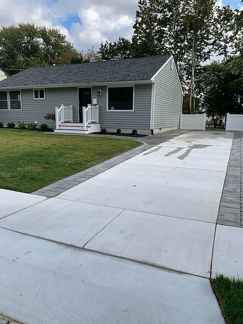 Front of the home, features concrete driveway with paver border. Paver walkway leads to front door.