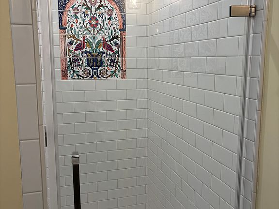 Tile shower with hand painted tile mural and frameless glass door