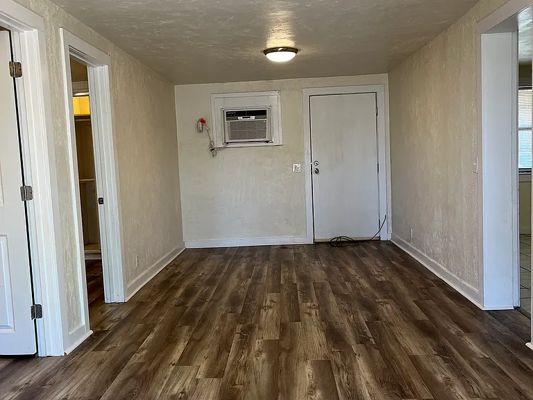 Living room as front door opens, showing doors on the left to the two bedrooms, and entry to the kitchen and bathroom to the right. Back door next to wall air/heat unit is a fire exit.