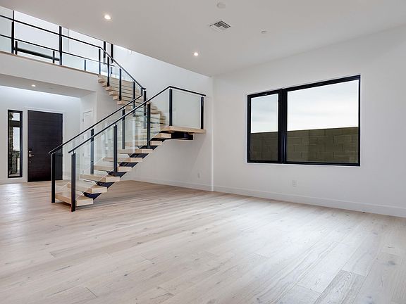 A modern, minimalist interior with a wooden floor, a staircase with a metal railing, and a large win