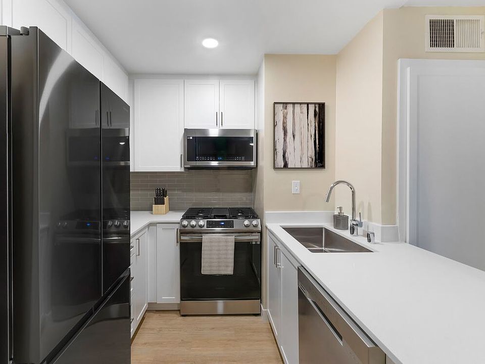 Renovated Package II kitchen with stainless steel appliances, white quartz countertops, white cabinetry, grey tile backsplash, and hard surface flooring