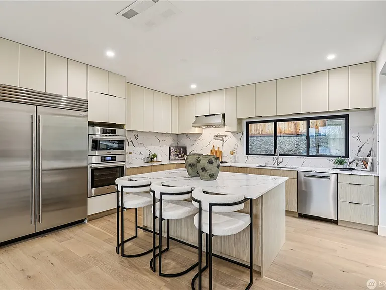 Gourmet chef's kitchen featuring a large quartz island with waterfall edges, sleek cabinetry, and stainless steel double ovens. Great open-concept flow.