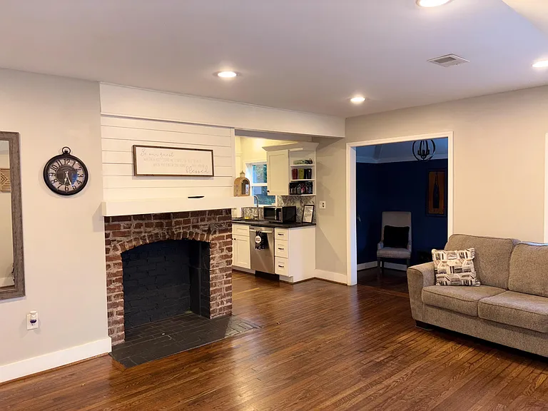 Open living area with hardwood floors, decorative brick fireplace, and convenient kitchenette with cabinet storage.