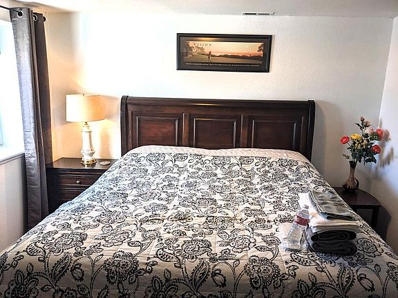 The king-size bed with linens supplied. On the left side is a large window with shade and curtains.