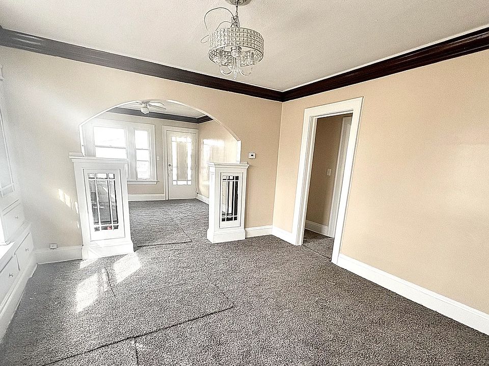 Unfurnished living room featuring a notable chandelier, arched walkways, crown molding, and baseboards