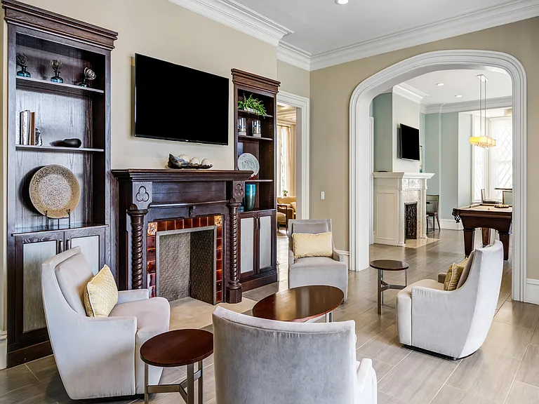 Luxurious living room featuring elegant chairs, a classic fireplace, built-in bookshelves, and seamless flow into an entertainment area with a pool table.