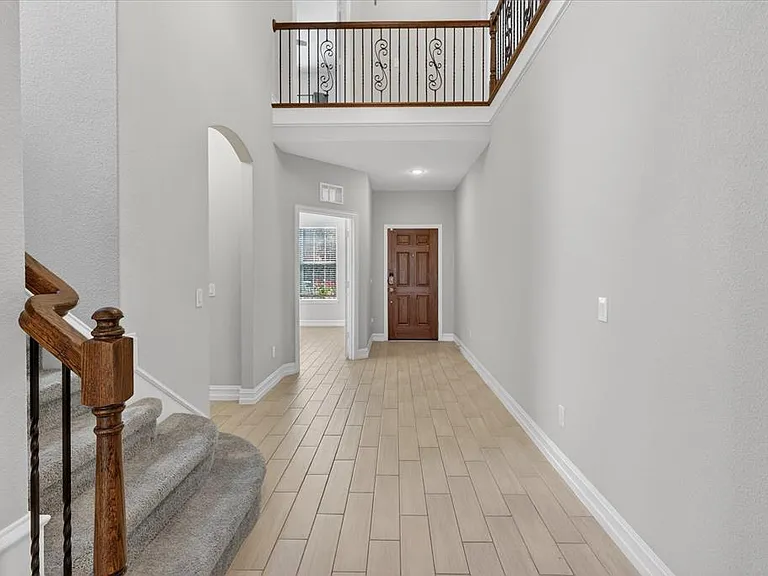 Two-story foyer featuring wood-finish tile flooring and a dark wood entry door