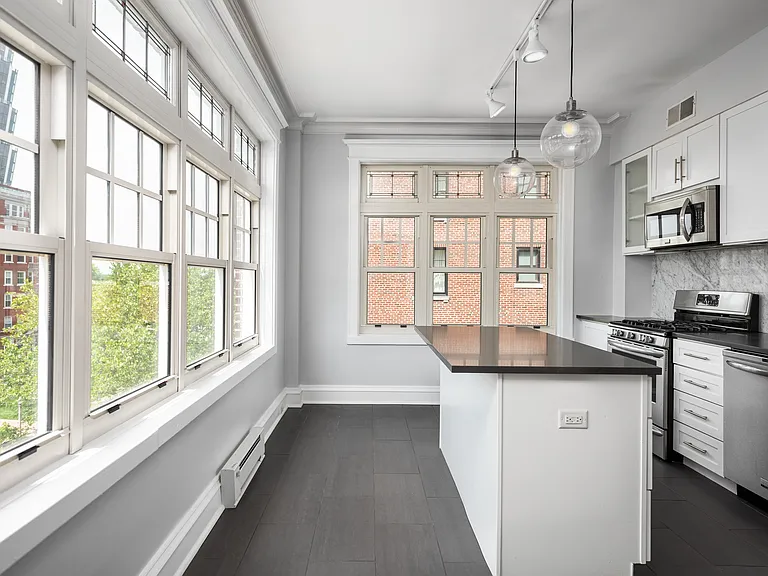 York House designer kitchen with gas stove, quartz countertops, stainless steel appliances, marble kitchen backsplash, and slate tile floor.