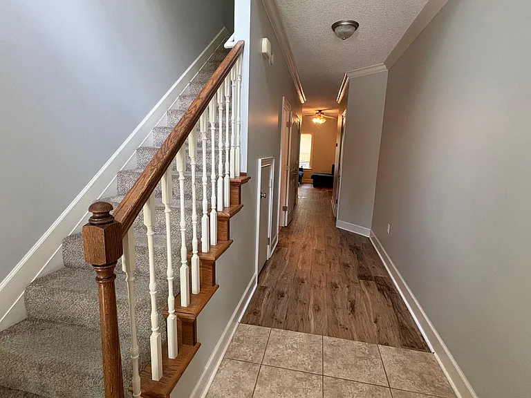 Long entry hallway with tile flooring, wood-style floors beyond, and a carpeted staircase with wood handrail.