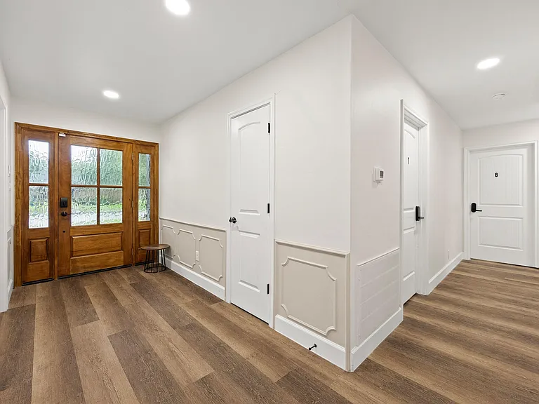 Wide entry hall with durable wood-look floors, paneled wainscoting, and a glass-inset front door for natural light.