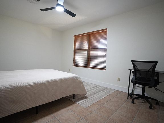 Spacious bedroom with a ceiling fan, large window with blinds, and a dedicated desk area for studying or remote work.