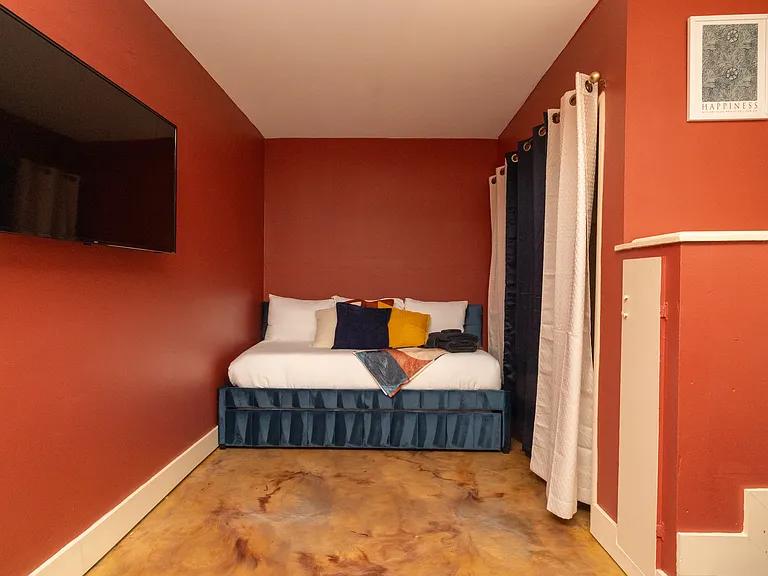 Warm and inviting bedroom featuring rich terracotta walls, a plush bed with colorful pillows, and a mounted TV_perfect for a cozy night in.