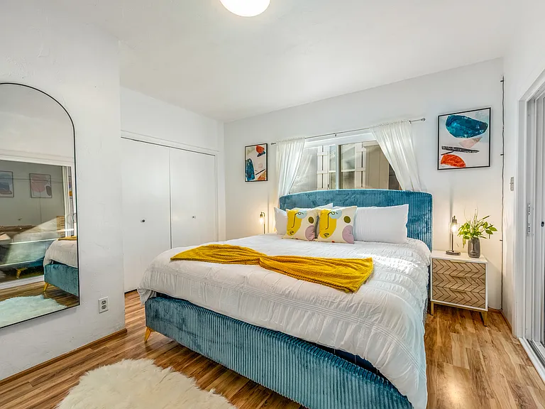Bathed in natural light from the large window, the room is accented with sleek nightstands, modern lamps, and tranquil artwork.