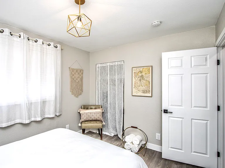 Cozy bedroom detail at Casa Del Sol, Tempe rental home. Features boho wall art, a vintage Arizona map, a leather accent chair, gold geometric lighting, fresh rolled towels, and a light-filled layout. Comfortable setup for a top Tempe, AZ stay.