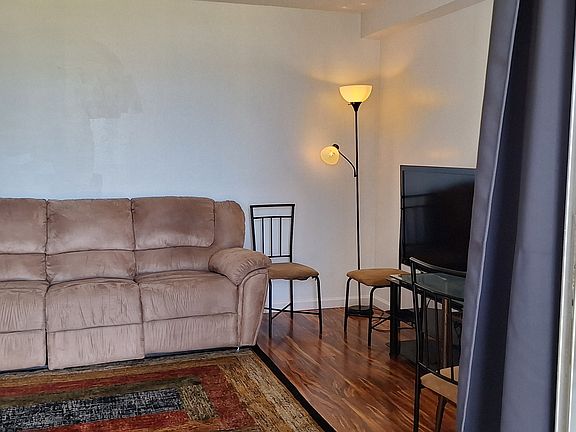 View from Lanai of the living room with couch where end seats have leg support. Also, partial view of the dining table and chairs, and lazy boy like chair.