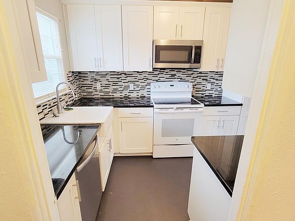 Kitchen with stainless steel dishwaser, white cabinets, microwave, granite counters