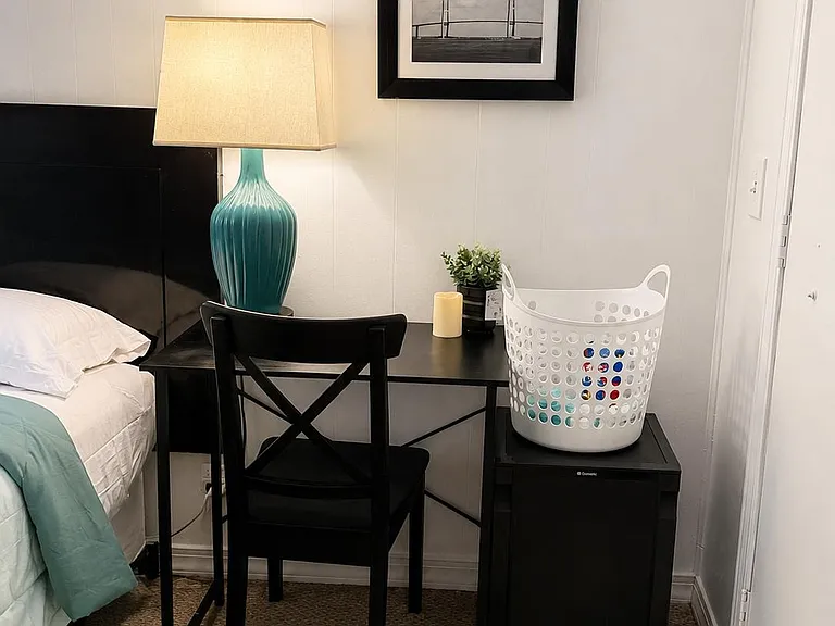 Furnished bedroom corner with a work desk and chair, bedside lighting, and an in-room mini fridge for added convenience.