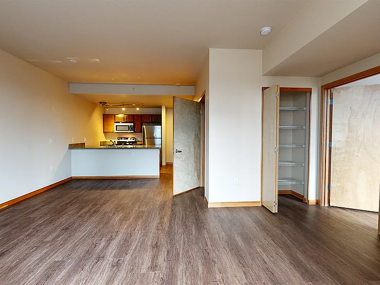 Apartment kitchen with stainless steel appliances, dining and living room with wood-style flooring.