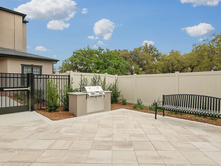 Inviting outdoor space with a modern grill, elegant bench, and lush greenery, perfect for entertaining under the open sky.