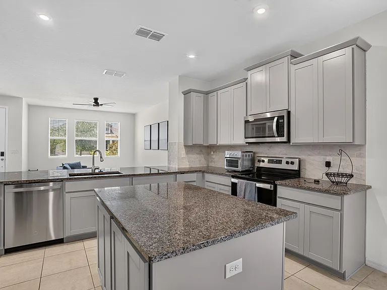 Open kitchen with a large island, granite counters, ample cabinetry, and stainless appliances, flowing into the main living a