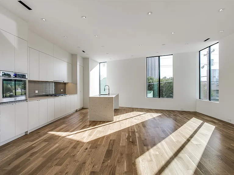 Open-concept kitchen and living area featuring wood-finish flooring, a kitchen island with sink, stainless steel appliances, white flat-panel cabinetry, and recessed lighting