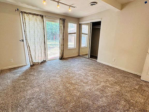 Spacious and inviting room with plush carpeting, modern track lighting, and large windows letting in natural light.