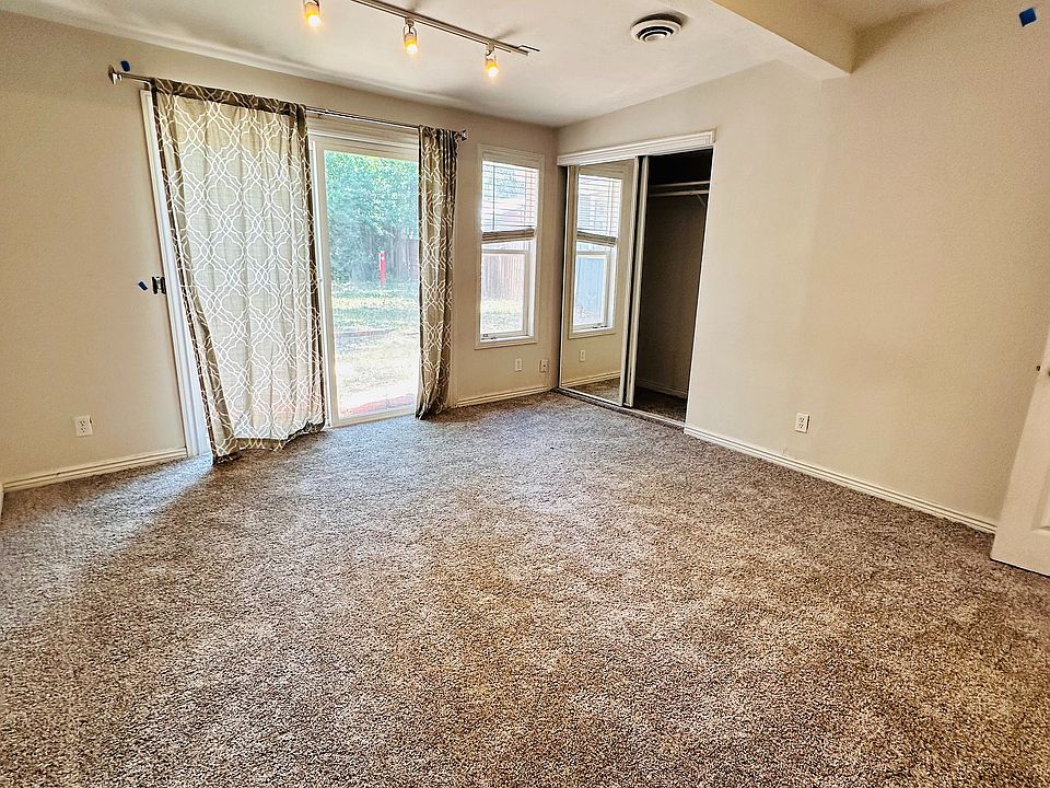 Spacious and inviting room with plush carpeting, modern track lighting, and large windows letting in natural light.
