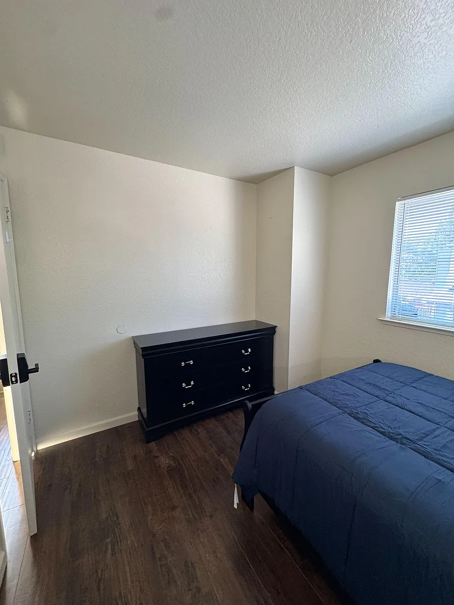 Private bedroom with wood-style flooring, a window with blinds, and space for a bed plus dresser or desk setup. - Calcutta Way