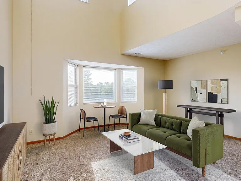 In the Madison, natural light fills the living room thanks to bay windows, soft carpet underfoot, and a spacious layout perfect for relaxing or entertaining.