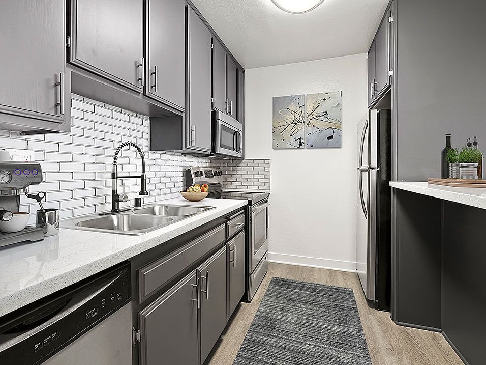 White tiled kitchen with stainless steel fridge, microwave, and oven.