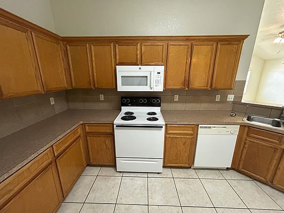 Spacious kitchen with tile floors, stainless steel sink and fridge, electric oven, over-the-range microwave, ample counter space, and a large pantry_perfect for cooking, storage, and everyday convenience.