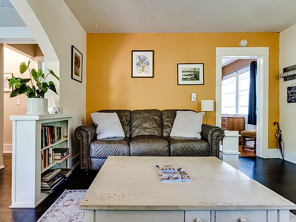 Living room features beautiful arch-way, hard wood floors, white brick fireplace with wood stove, fresh paint (2023) and beautiful built-in bookshelves.