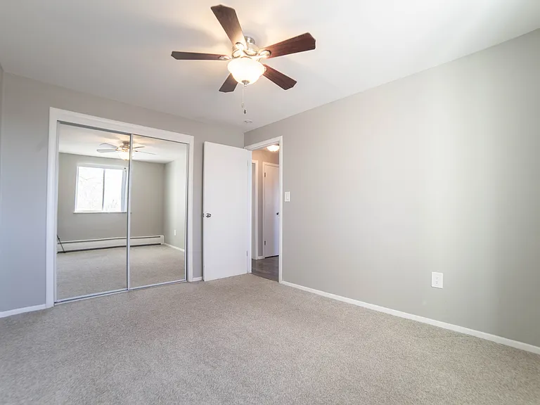 Bright and airy bedroom with plush carpeting, mirrored closet doors, and a modern ceiling fan.
