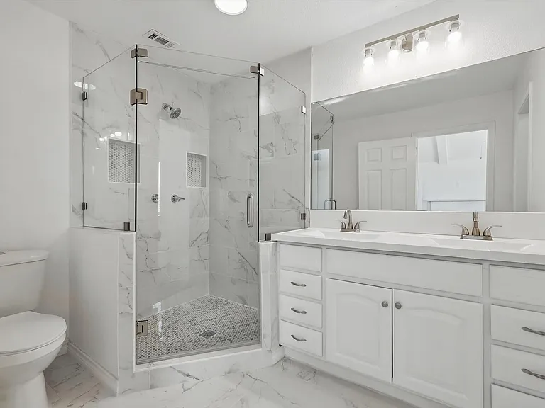 Full bathroom with marble look tiles, a marble finish shower, double vanity, toilet, and baseboards