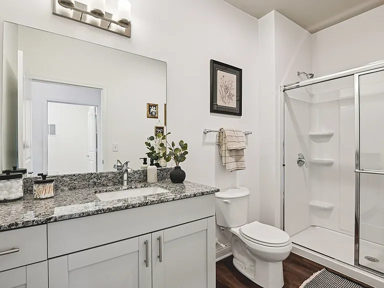 Step into a refined, high-end space defined by sharp lines, a bold granite vanity, and a glass-enclosed shower.