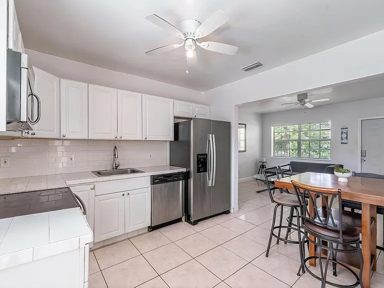 Open-concept kitchen with ample white cabinetry, tile backsplash, stainless appliances, and an adjacent dining area.