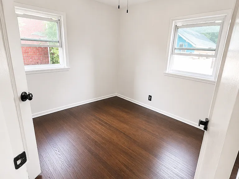 Comfortable second bedroom with hardwood floors, two windows, and ceiling fan.