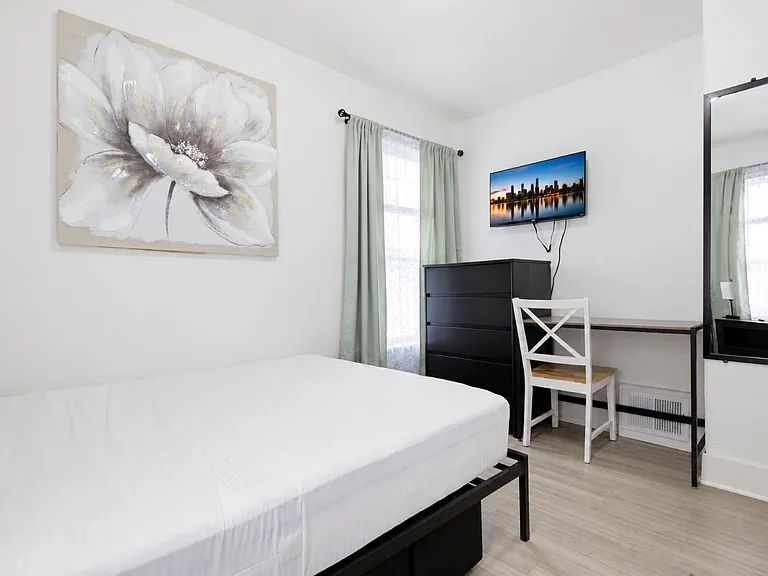 Private bedroom with a full bed, dresser, and dedicated desk setup, plus a large mirror and window with curtains.