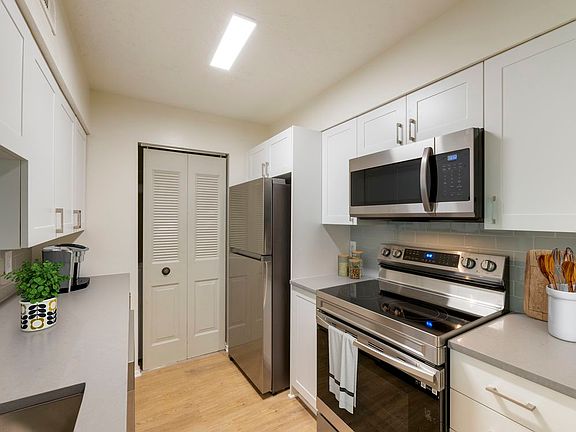 Renovated Meadows II kitchen with stainless steel appliances, white cabinetry, grey quartz countertops, grey tile backsplash, and hard surface flooring