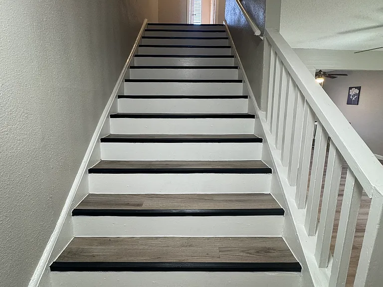 This updated staircase showcases contemporary wood_textured steps with crisp white risers and leads to a naturally lit upper hallway.