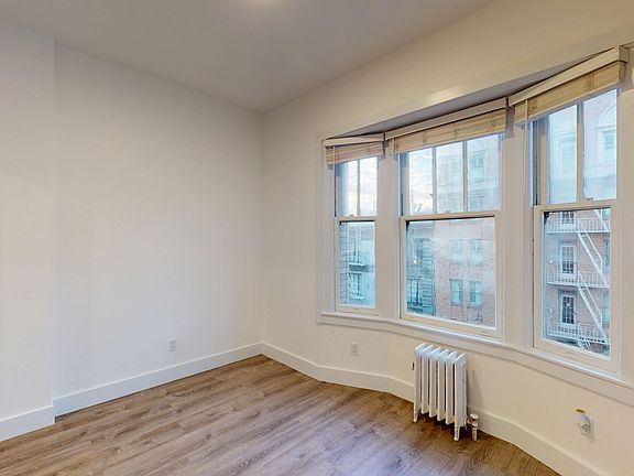 Room with bay window, blinds, wood floor, and radiator below