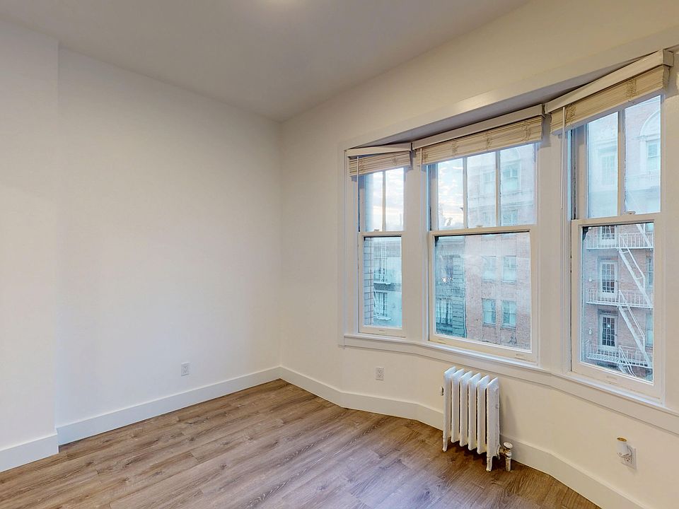 Room with bay window, blinds, wood floor, and radiator below
