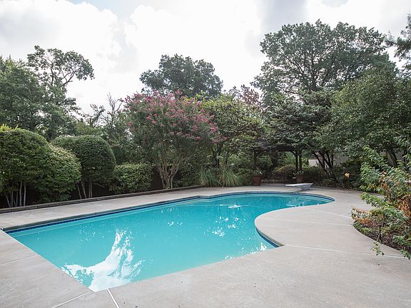 Sparkling diving pool is surrounded by mature landscape including shade trees, gorgeous perennials and custom pergola with fan.