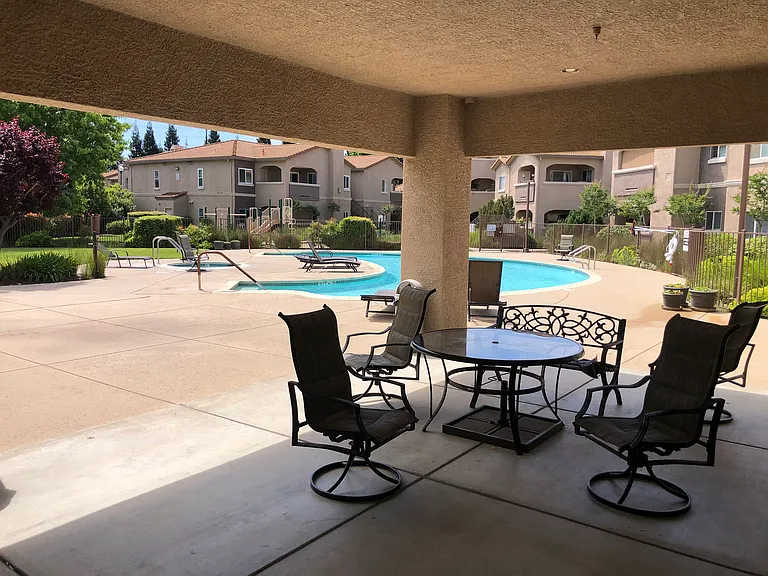 Covered patio in pool area with tables and chairs. Also outside shower located in pool area.