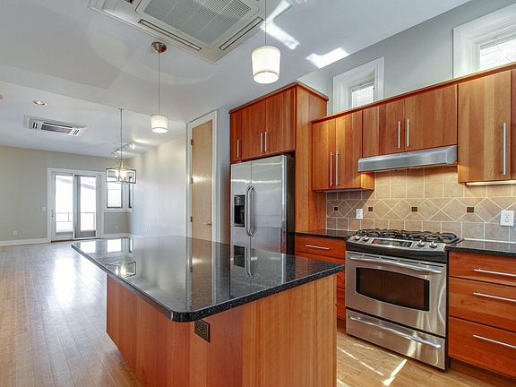 Kitchen view from front door with all stainless steel appliances and wood flooring.