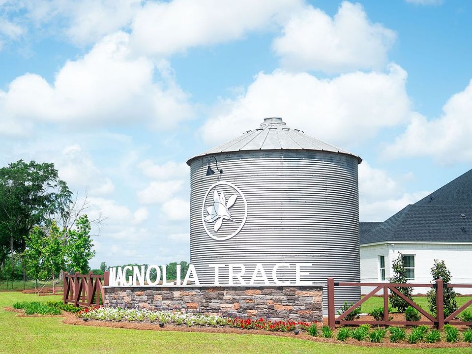 Magnolia Trace entrance silo with signage, fencing, and landscaped greenery near new homes